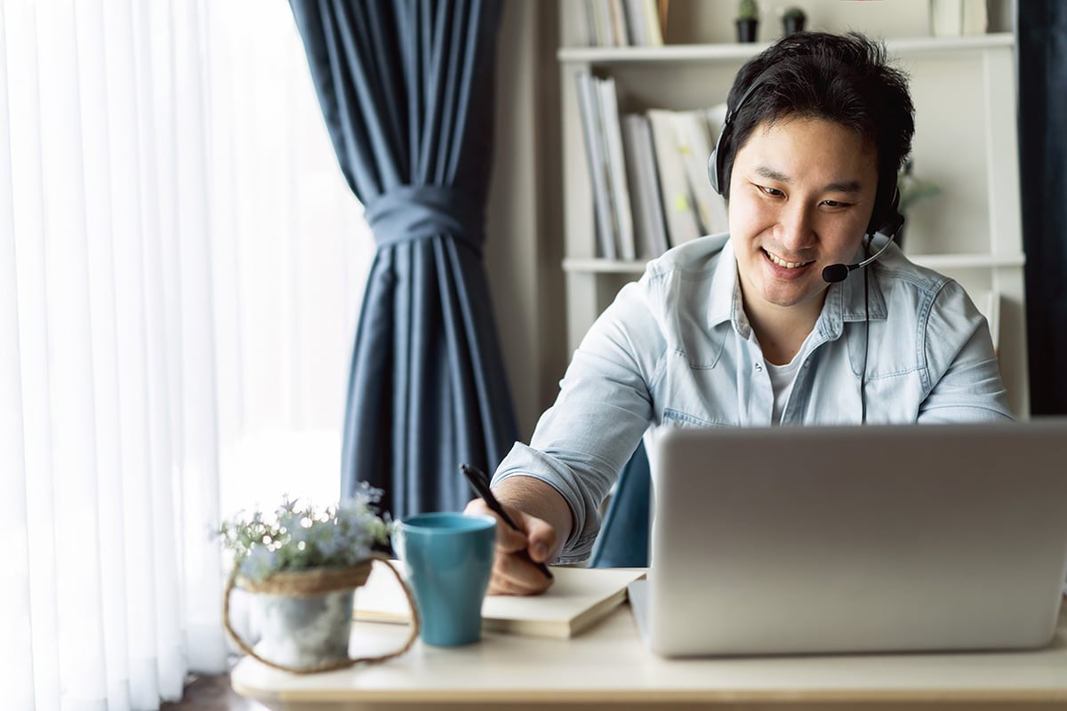 A man smiling and taking notes while working on his laptop