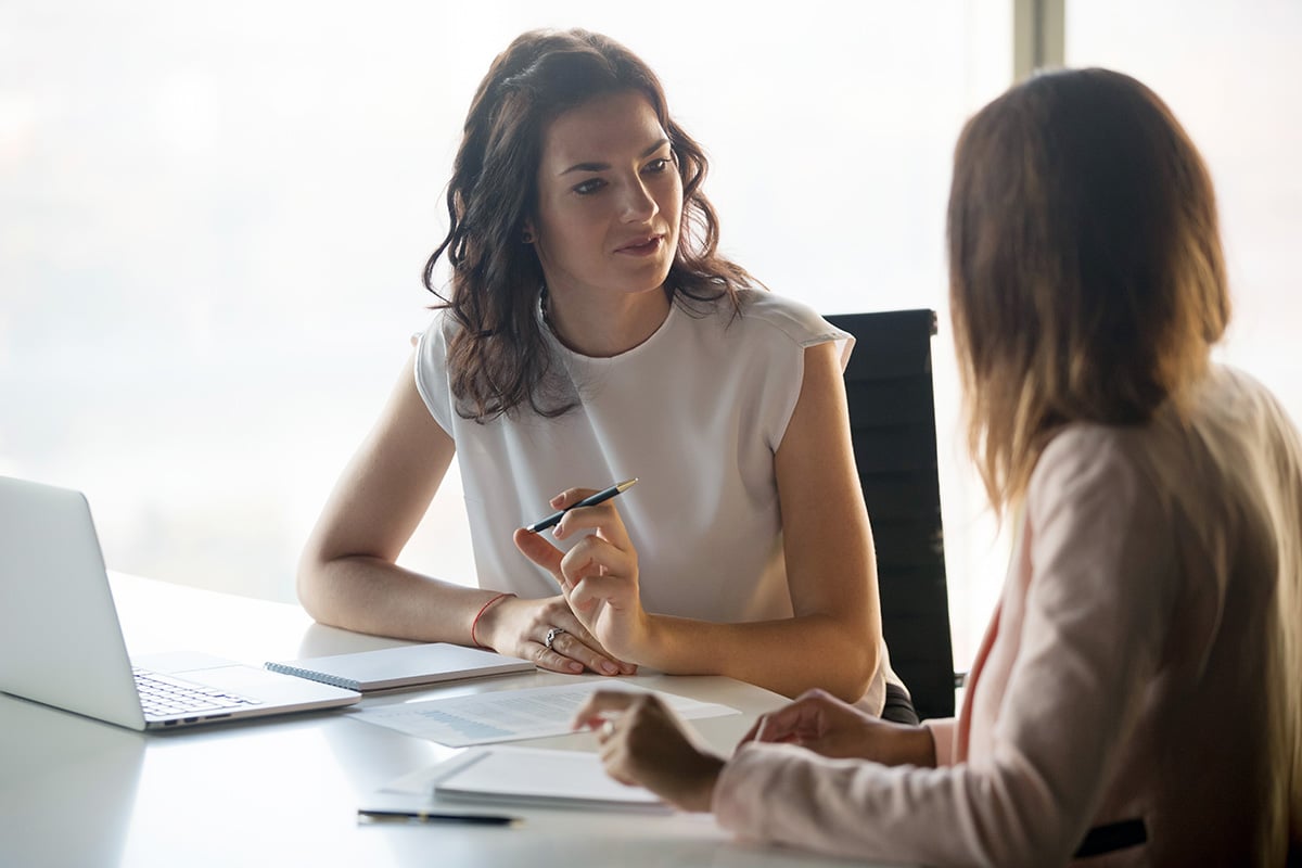 Two women talking in front of a table with a laptop