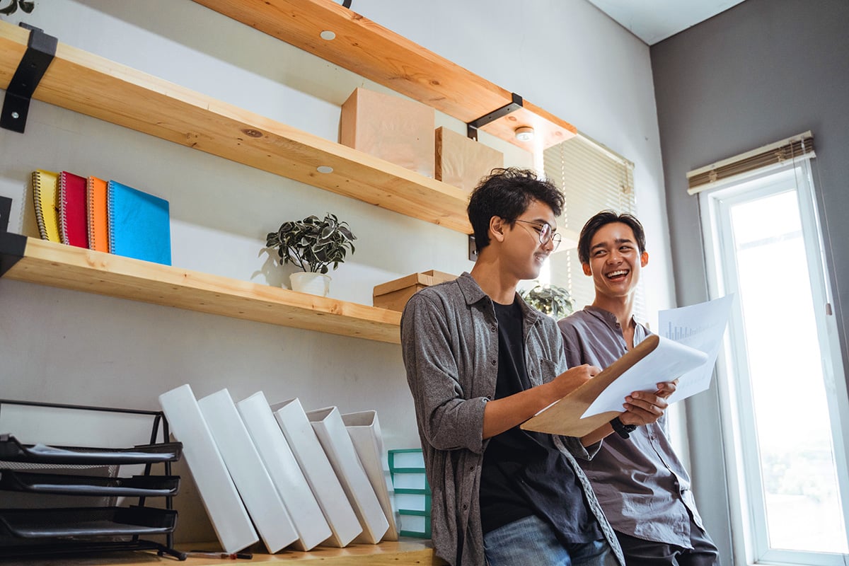 Two male colleagues looking at a clipboard and laughing