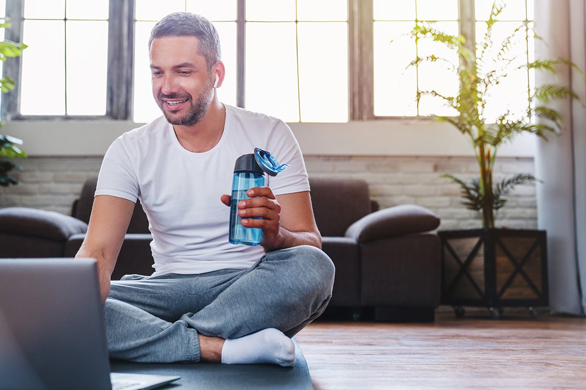 Man looking at his laptop after a workout with a bottle of water in his hand