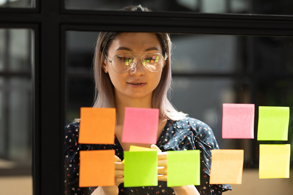 Woman looking at a glass wall with post-it notes stuck on it